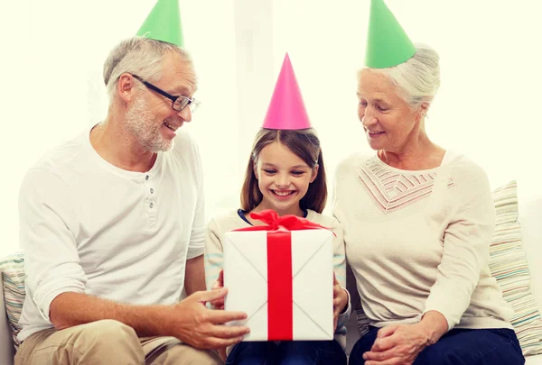 Famiglia sorridente in cappelli da festa con scatola regalo a casa — Foto Stock