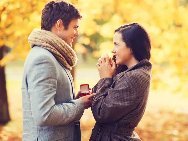 Coppia sorridente con confezione regalo rossa nel parco autunnale — Foto Stock