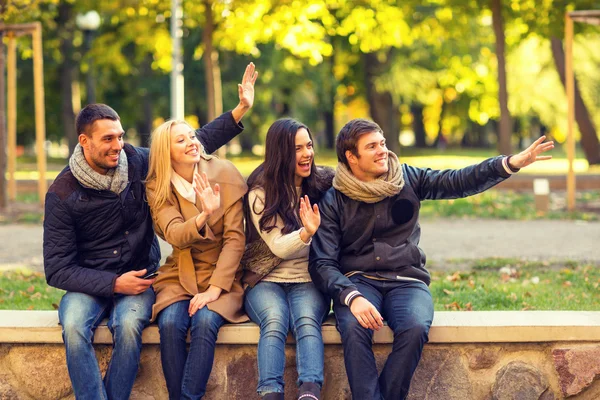 Группа улыбающихся друзей, машущих руками в городском парке — стоковое фото