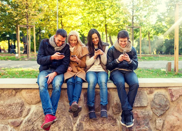 Amigos sonrientes con teléfonos inteligentes en el parque de la ciudad —  Fotos de Stock