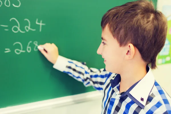Piccolo scolaro sorridente che scrive su lavagna di gesso — Foto Stock