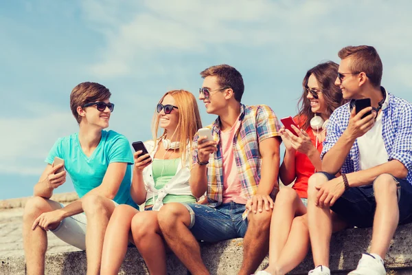 Grupo de amigos sonrientes con teléfonos inteligentes al aire libre — Foto de Stock