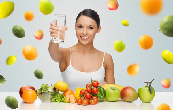 Mulher feliz com comida saudável mostrando vidro de água — Fotografia de Stock