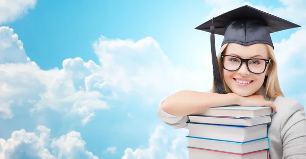 Estudante em trencher cap com livros sobre céu azul — Fotografia de Stock