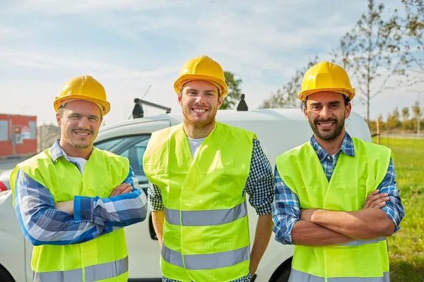 Gelukkige mannelijke bouwers in hoog zichtbare vesten buiten — Stockfoto