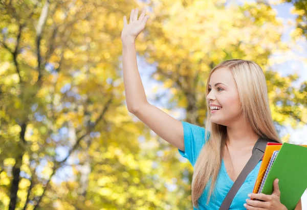 Student with folders waving hand over autumn park — Zdjęcie stockowe
