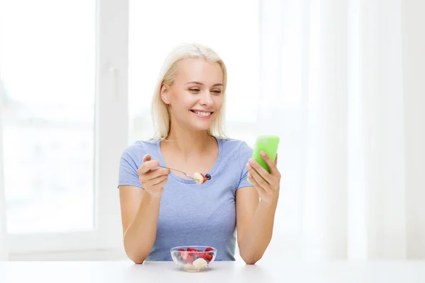 Vrouw met smartphone eten vruchten thuis — Stockfoto