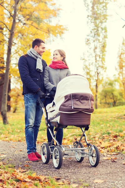 Smiling couple with baby pram in autumn park — Stock Photo, Image