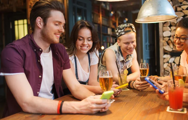 Gelukkige vrienden met smartphones en drankjes in bar — Stockfoto