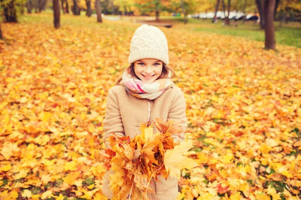 Ragazzina sorridente con foglie autunnali nel parco — Foto Stock