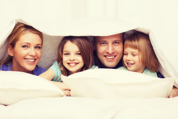 Família feliz com dois filhos sob cobertor em casa — Fotografia de Stock