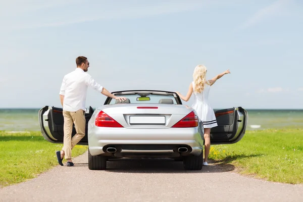 Happy man and woman near cabriolet car at sea — Stock Photo, Image