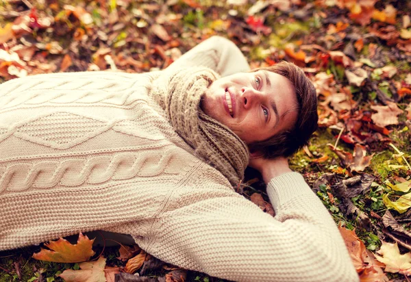 Close up of smiling young man lying in autumn park — Stock Photo, Image
