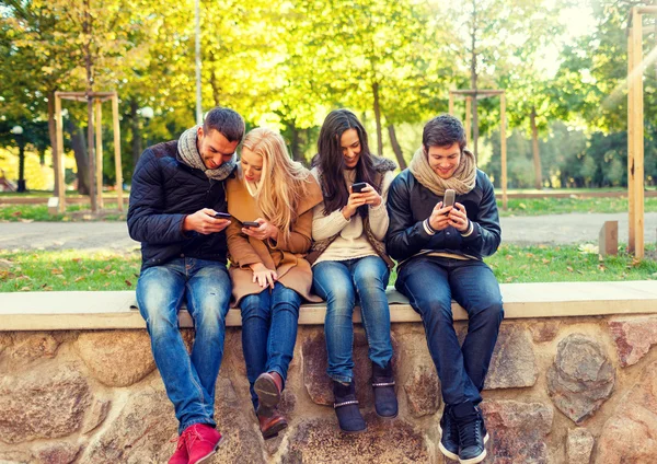 Amigos sonrientes con teléfonos inteligentes en el parque de la ciudad —  Fotos de Stock