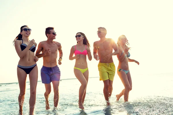 Amis souriants dans des lunettes de soleil courir sur la plage — Photo