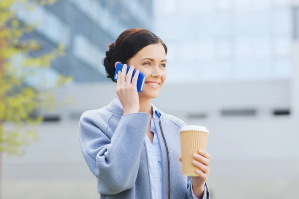 Улыбающаяся женщина с кофе звонит на смартфон — стоковое фото