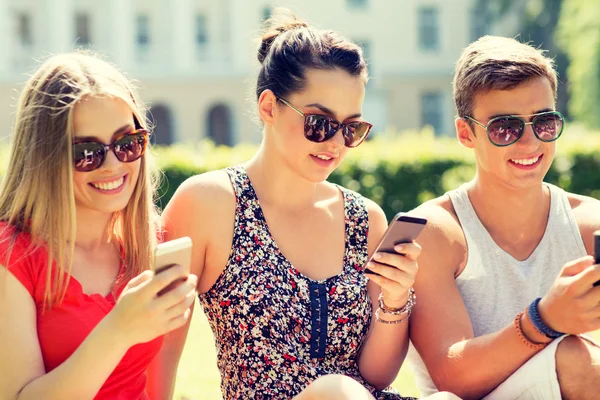 Amigos sonrientes con teléfonos inteligentes sentados en la hierba —  Fotos de Stock