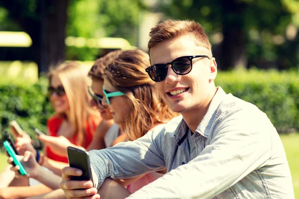 Amigos sorridentes com smartphones sentados no parque — Fotografia de Stock
