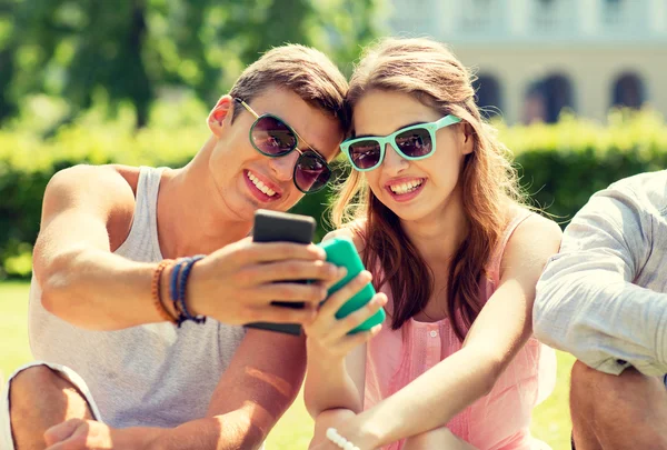 Amigos sonrientes con teléfonos inteligentes sentados en el parque — Foto de Stock