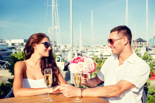 Smiling couple with bunch and champagne at cafe — Stock Photo, Image