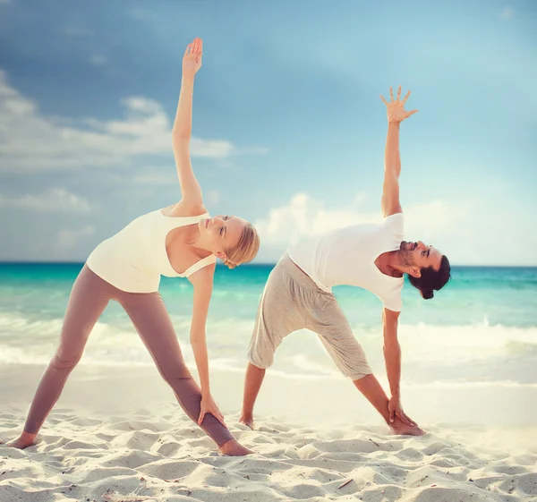 Pareja haciendo ejercicios de yoga en la playa de verano —  Fotos de Stock