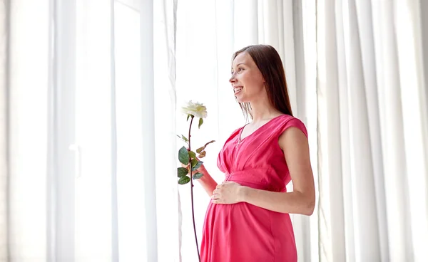 Ευτυχισμένη έγκυος γυναίκα με το ροδαλό λουλούδι στο σπίτι — Φωτογραφία Αρχείου