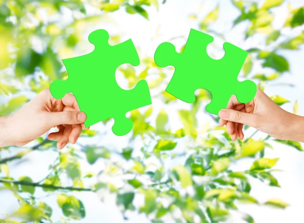 Mãos com quebra-cabeça verde sobre fundo natural — Fotografia de Stock