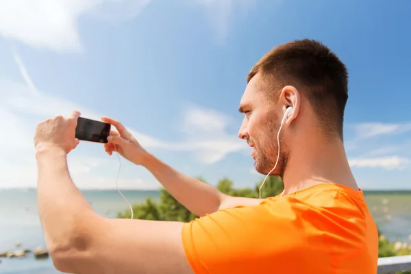 Smiling young man with smartphone and earphones — Stock Photo, Image