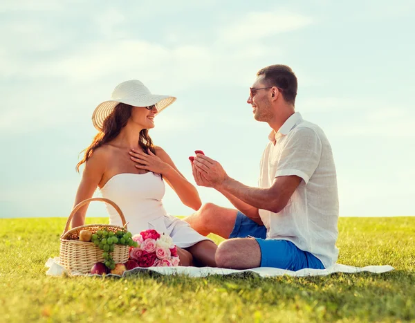 Sonriente pareja con pequeña caja de regalo roja en el picnic —  Fotos de Stock