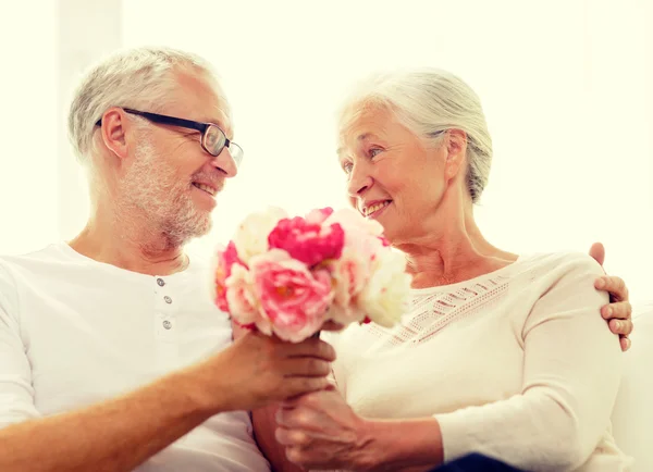 Happy senior couple with bunch of flowers at home — Stock Photo, Image