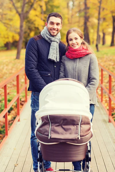 Smiling couple with baby pram in autumn park — Stock Photo, Image