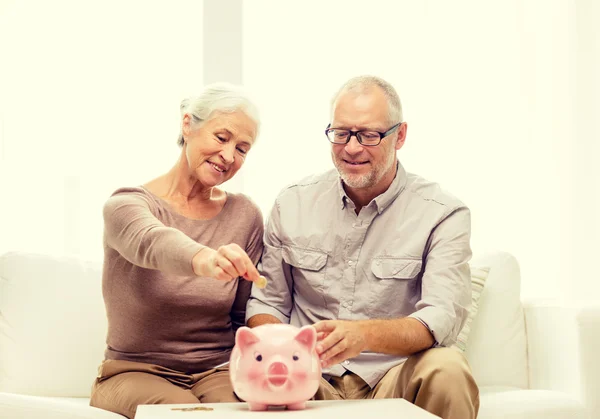 Casal sênior com dinheiro e banco porquinho em casa — Fotografia de Stock