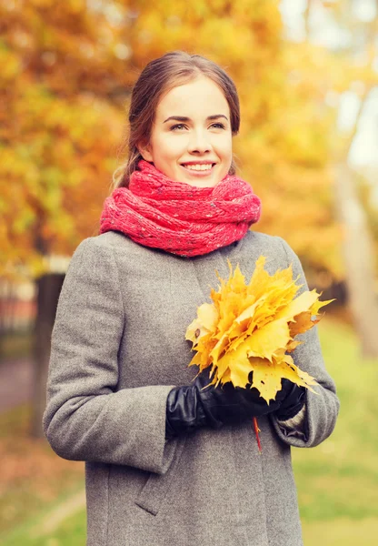 Mujer sonriente con racimo de hojas en el parque de otoño —  Fotos de Stock