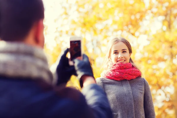 Casal sorridente com smartphone no parque de outono — Fotografia de Stock