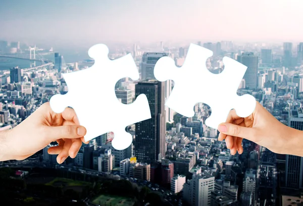 Hands with green puzzle over city background — Stock Photo, Image