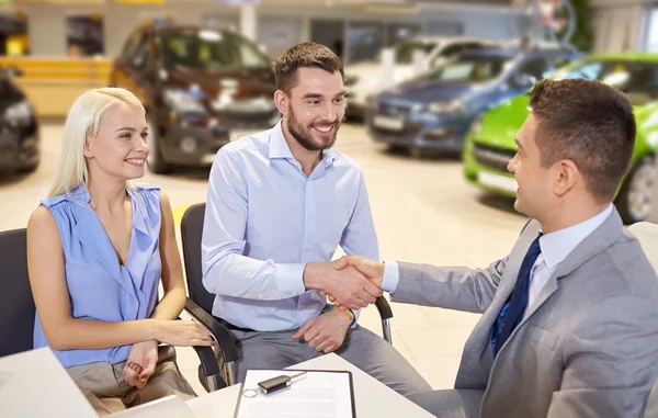 Glückliches Paar mit Autohändler in Auto-Show oder Salon — Stockfoto