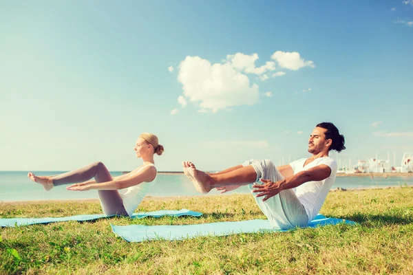 Sorrindo casal fazendo exercícios de ioga ao ar livre — Fotografia de Stock