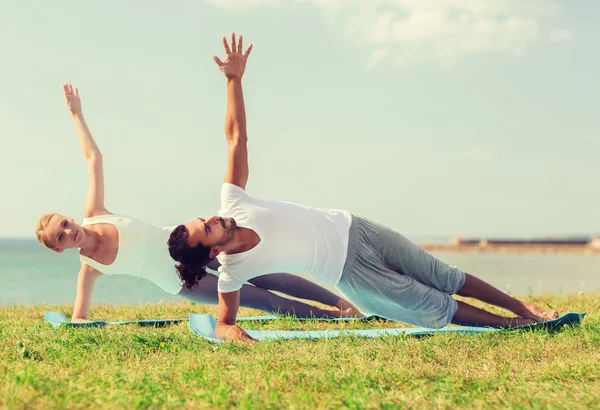 Улыбающаяся пара делает упражнения для йоги на открытом воздухе — стоковое фото