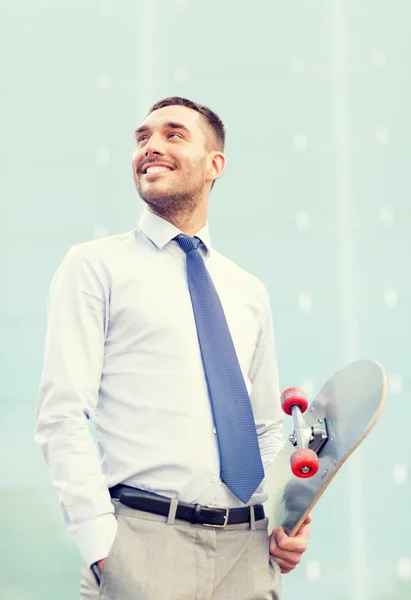 Joven hombre de negocios sonriente con monopatín al aire libre — Foto de Stock
