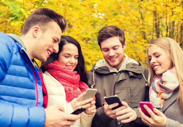 Amigos sonrientes con teléfonos inteligentes en el parque de la ciudad — Foto de Stock