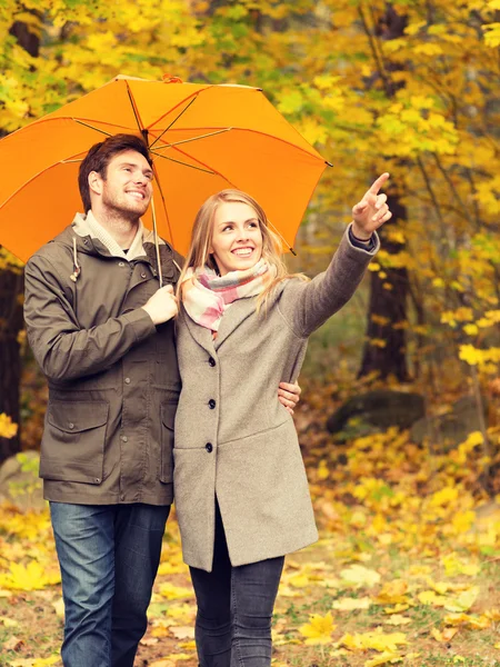 Coppia sorridente con ombrellone nel parco autunnale — Foto Stock