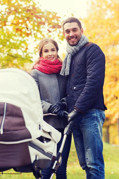 Smiling couple with baby pram in autumn park — Stock Photo, Image