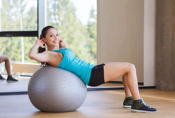 Uśmiechnięta kobieta z fit ball wyginanie mięśni w siłowni — Zdjęcie stockowe