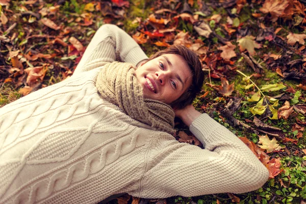 年轻的男人微笑着，躺在一片秋色的公园的特写 — 图库照片