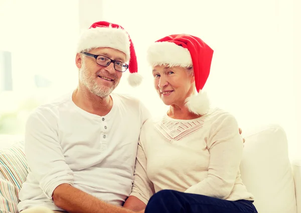 Feliz casal sênior em santa helper chapéus em casa — Fotografia de Stock