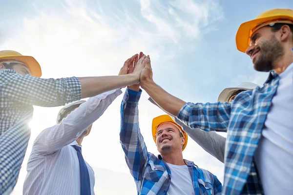 Close up of builders in hardhats making high five — Stock Photo, Image
