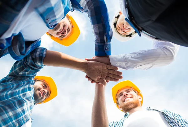 Close up of builders in hardhats with hands on top — Stock Photo, Image