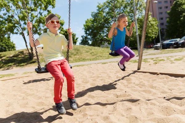 Dos niños felices balanceándose en el columpio en el patio de juegos —  Fotos de Stock