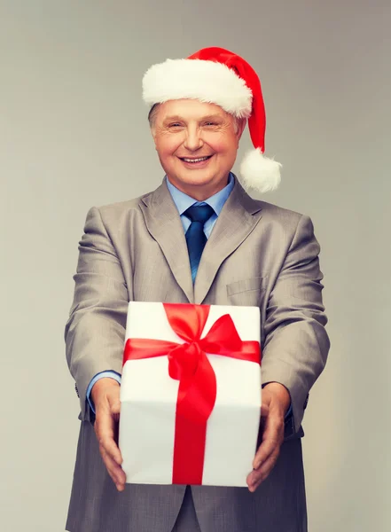 Takım elbise ve santa yardımcı şapkalı hediye ile gülümseyen adam — Stok fotoğraf