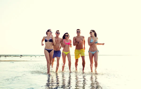 Amigos sonrientes en gafas de sol corriendo en la playa — Foto de Stock